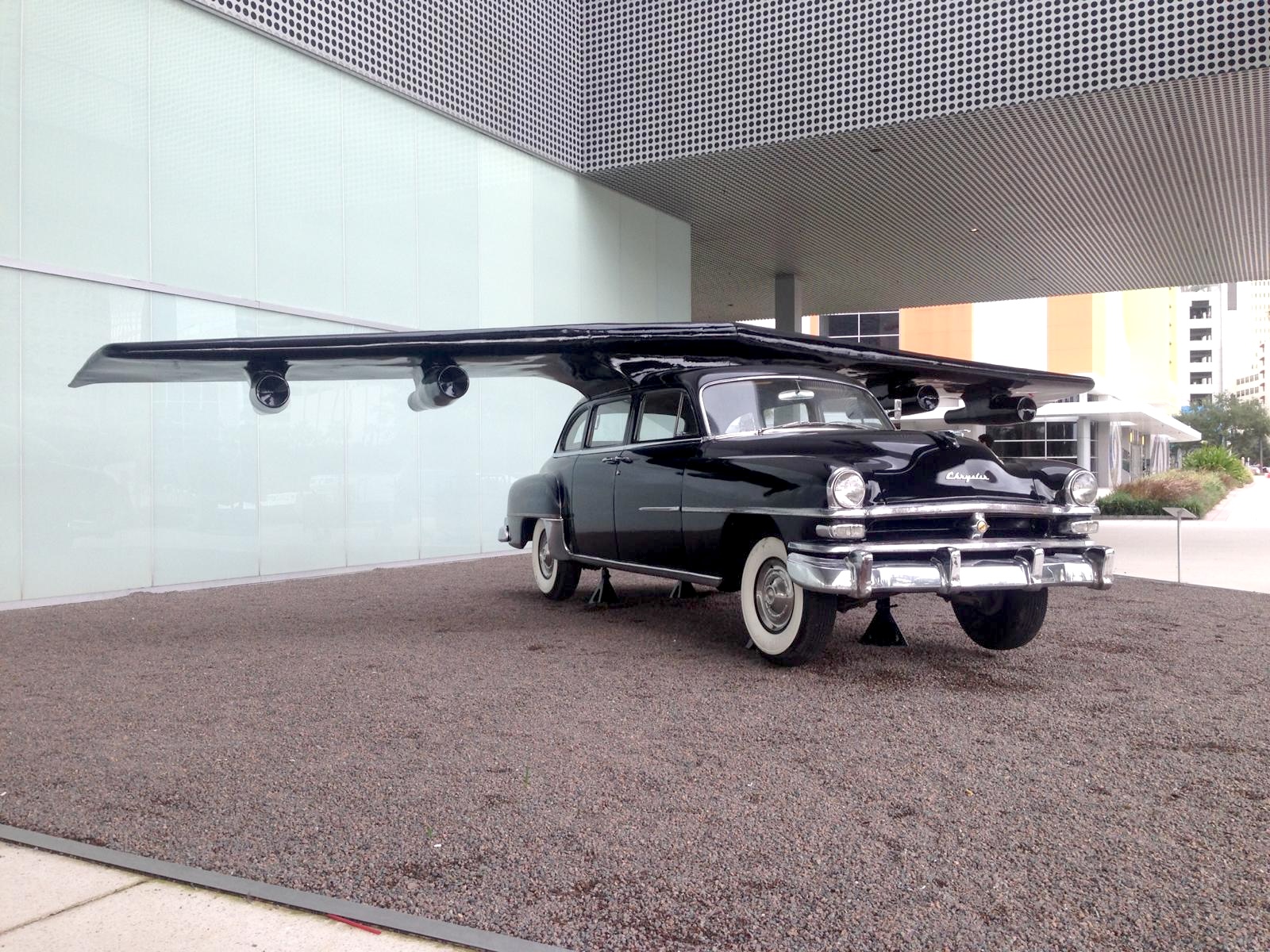 The sculpture displayed on gravel outside a modern museum building with a perforated metal facade.