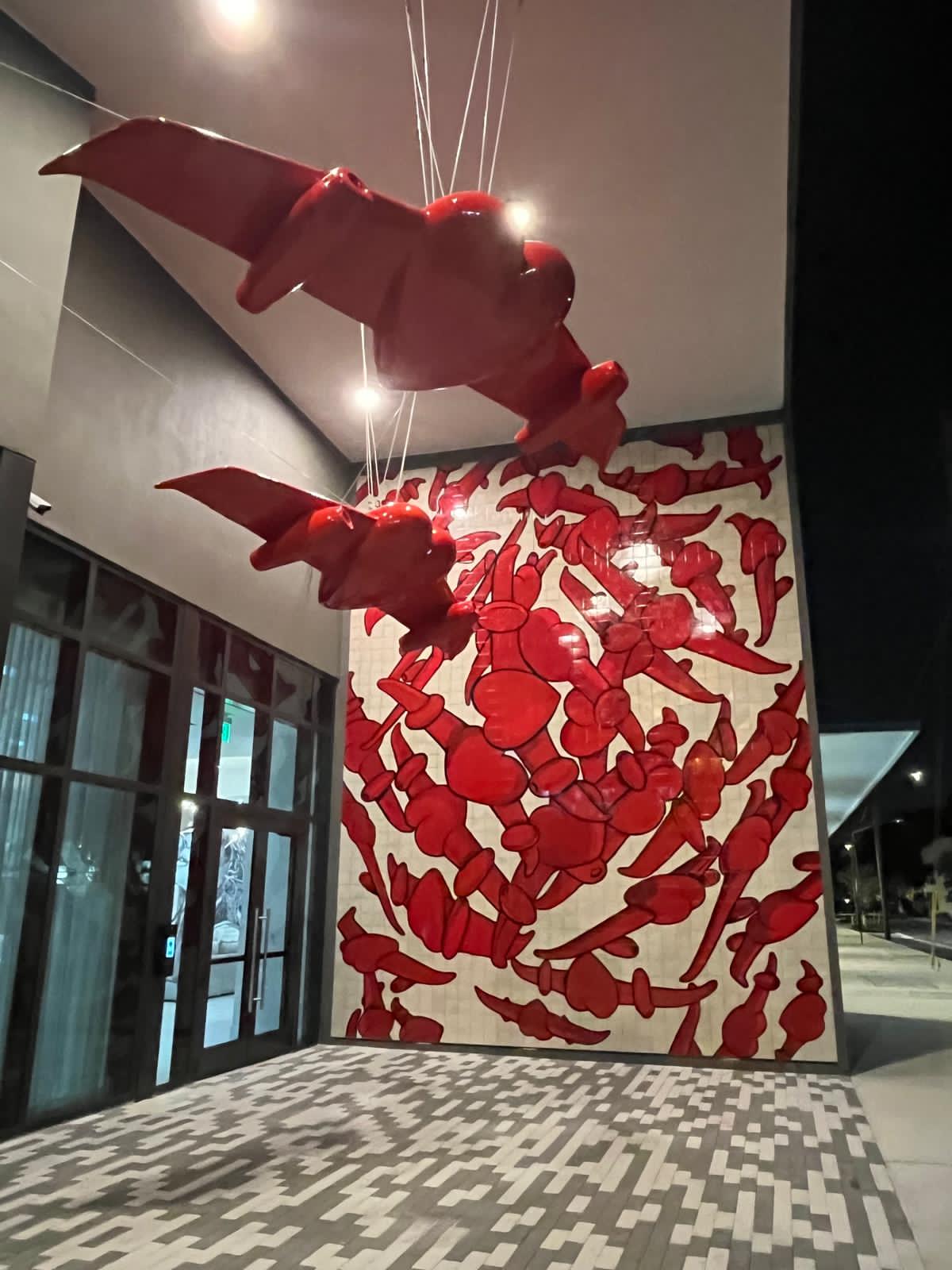Nighttime view of the two winged-heart sculptures and matching red tile mural, illuminated at the building entrance.