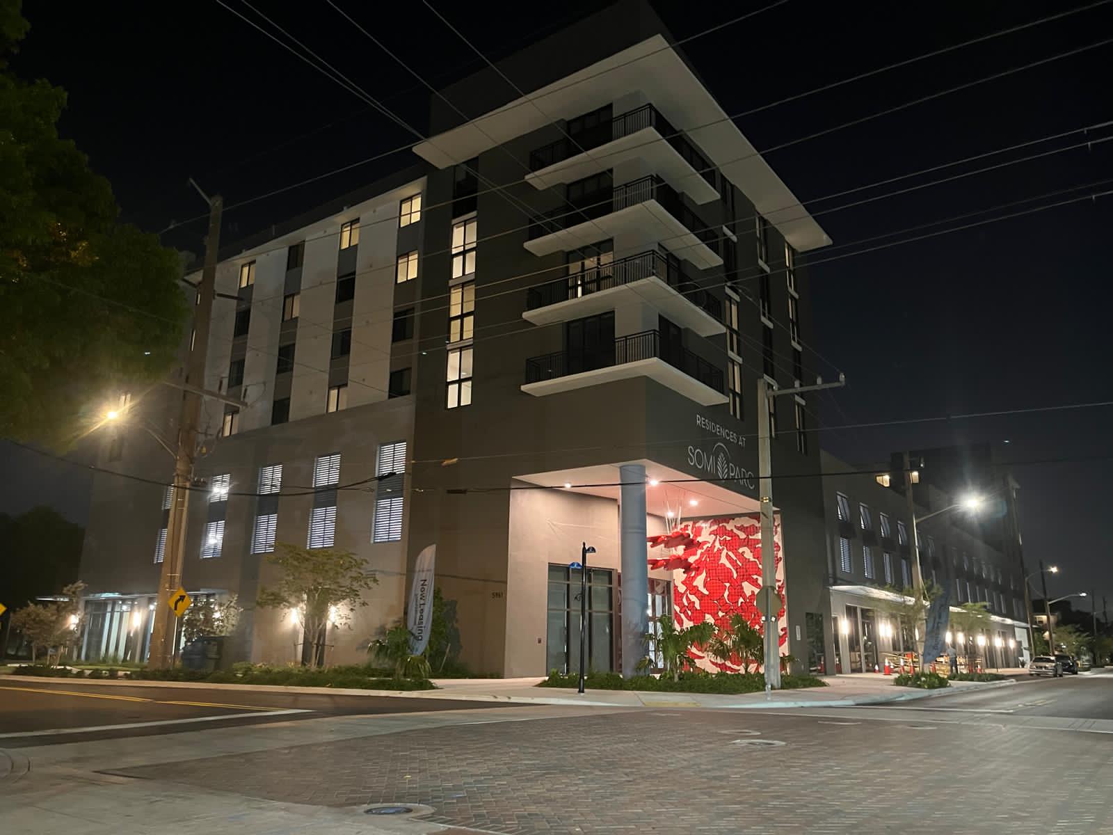 Night view of the full Residences at SoMi Parc apartment building, with the red tile mural visible at the entrance corner.