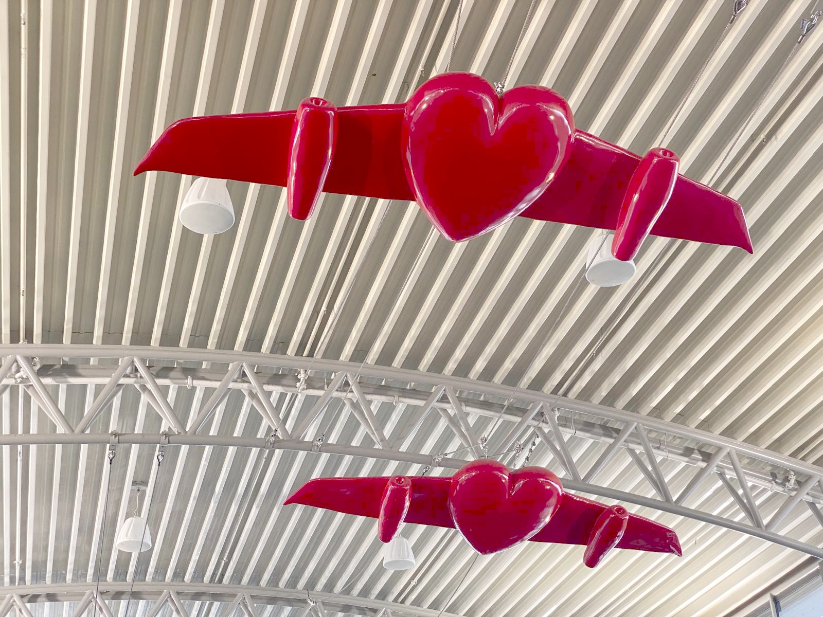 Close-up of two winged-heart sculptures against the airport's corrugated metal roof structure.