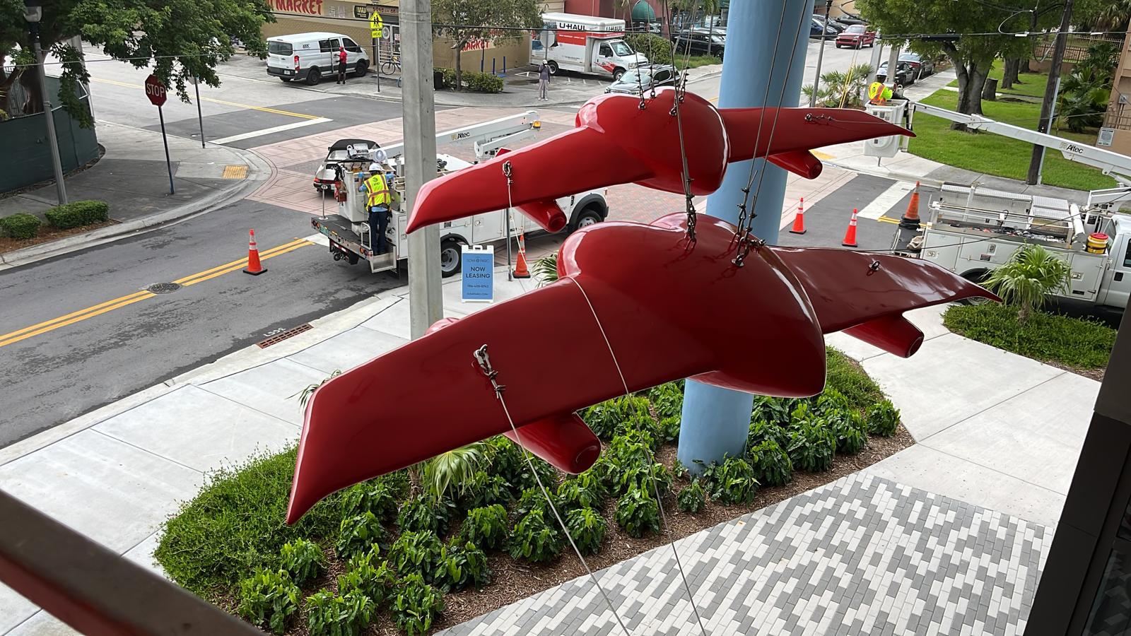 Daytime installation of the two winged-heart sculptures with a bucket truck, seen from above at the street corner.