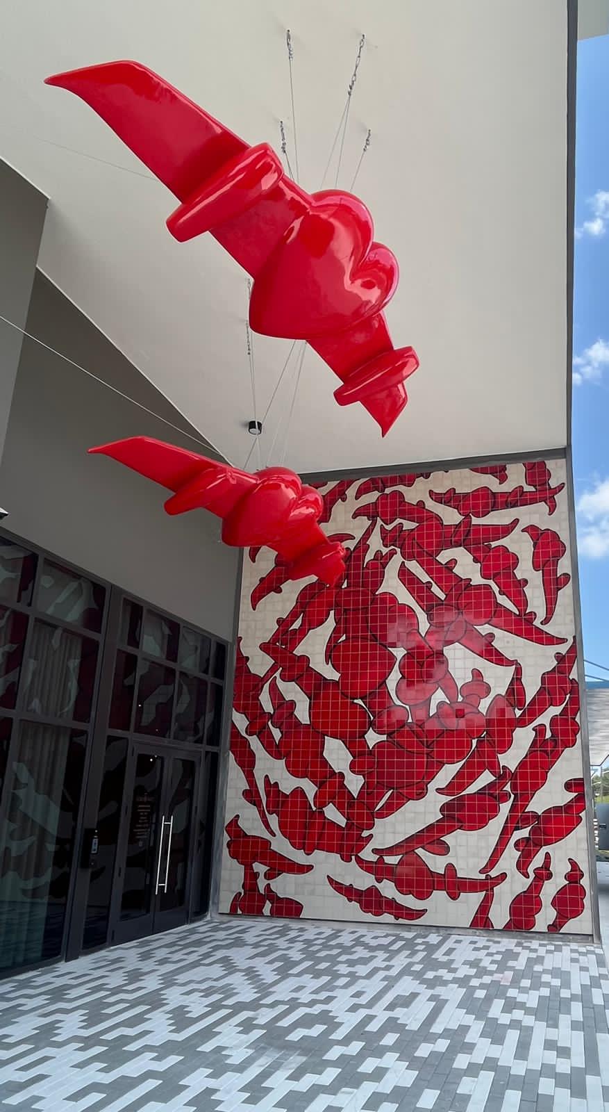 Vertical daytime view from beneath the entrance canopy, showing both winged-heart sculptures and the full tile mural.