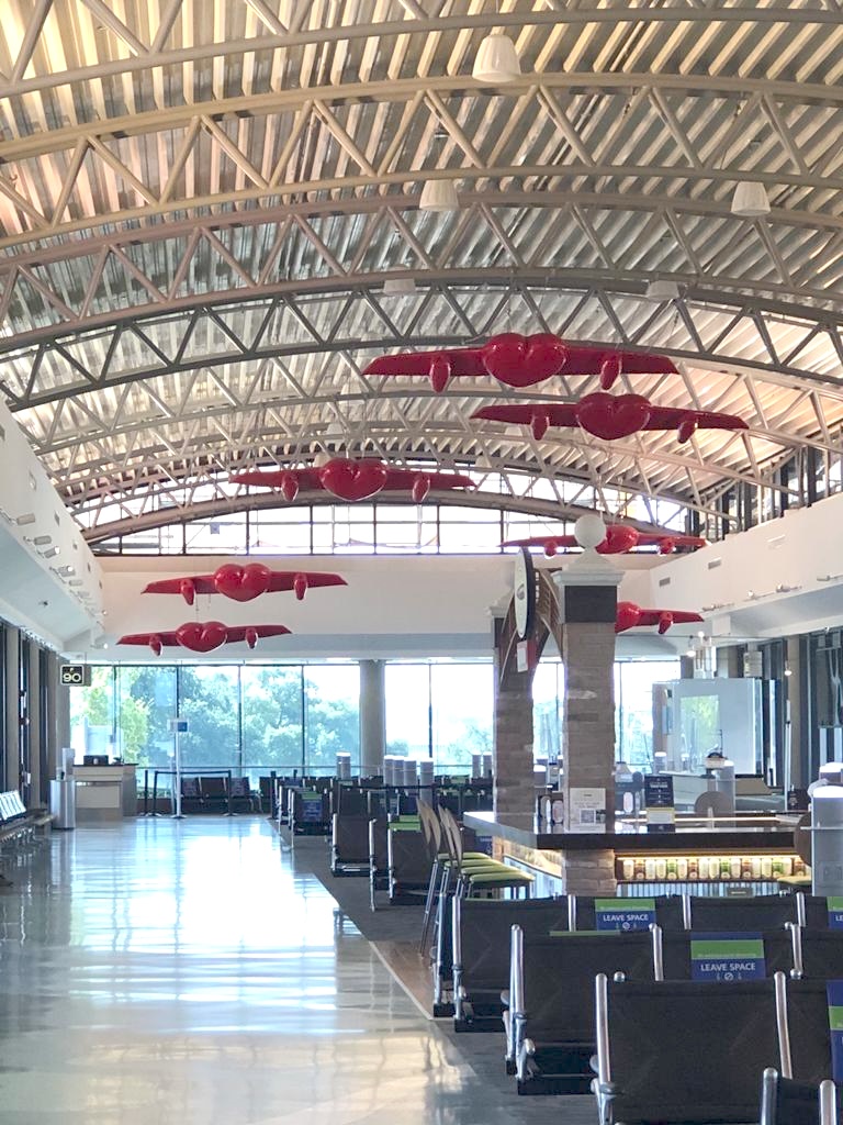 Wide view of the airport terminal's vaulted steel ceiling with multiple winged-heart sculptures suspended above the seating area.