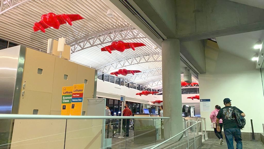 Winged-heart sculptures hanging above the airport's check-in area, near Lufthansa signage.