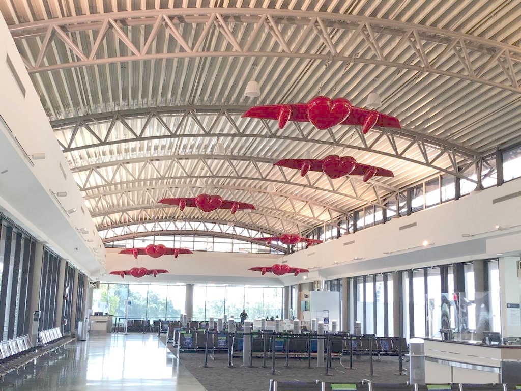 A long row of winged-heart sculptures suspended along the length of the airport terminal's vaulted ceiling.