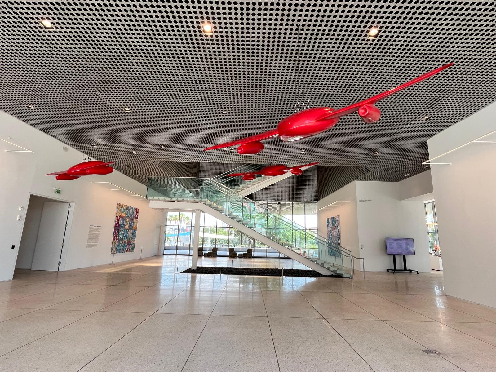 Museum lobby view of the winged-heart sculptures suspended above the main staircase, with paintings on the side walls.