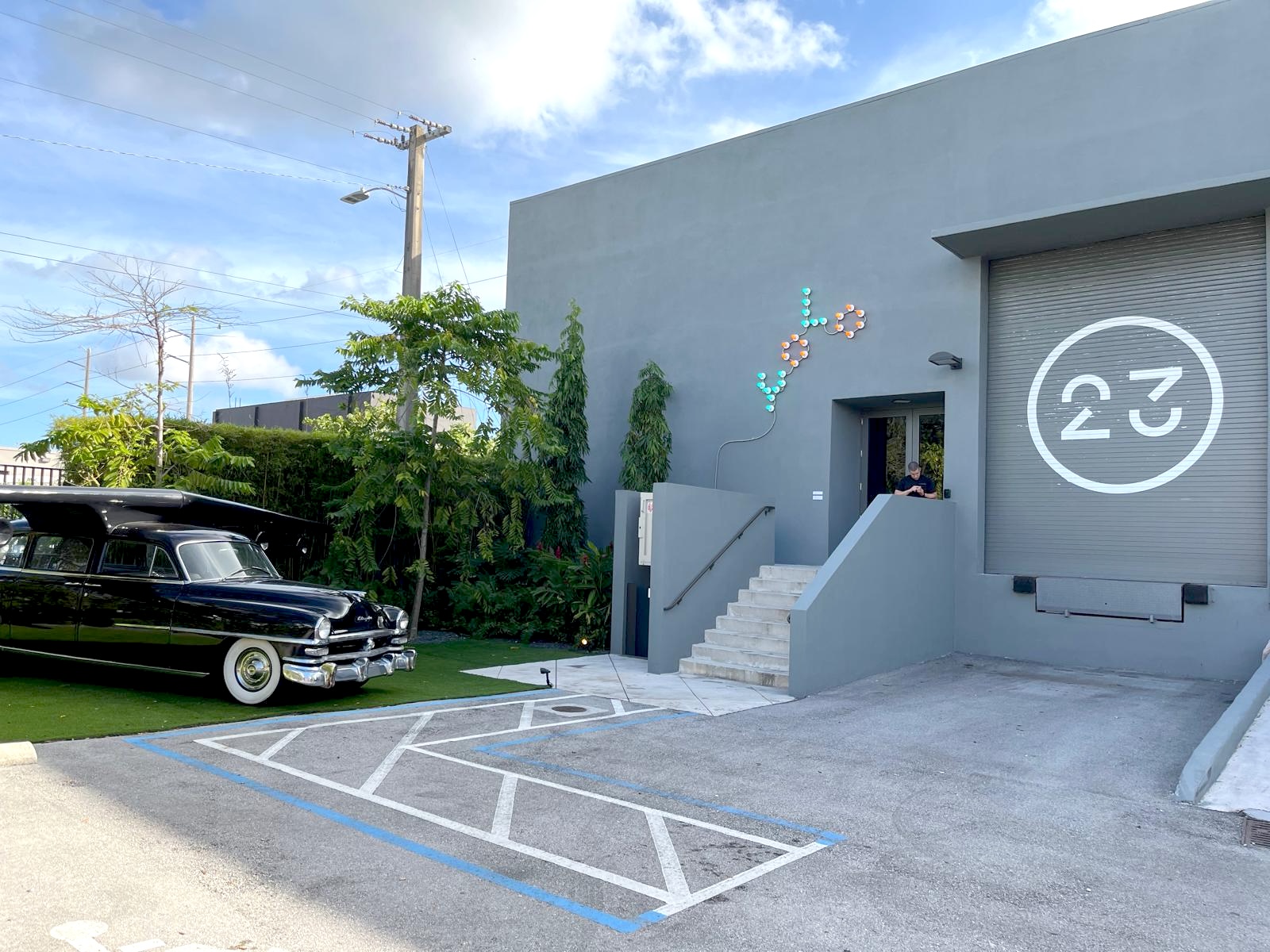 The sculpture parked beside a modern gray building with a large circular '23' logo painted on its loading door.