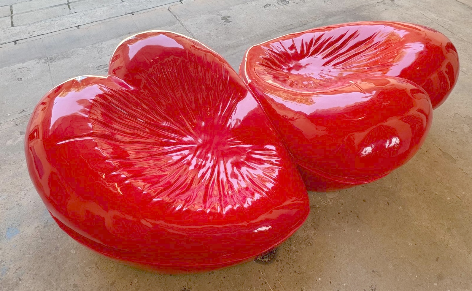 Two glossy red fiberglass sculptures with radiating starburst-textured hollows, resembling large bisected fruit, on a paved outdoor surface.