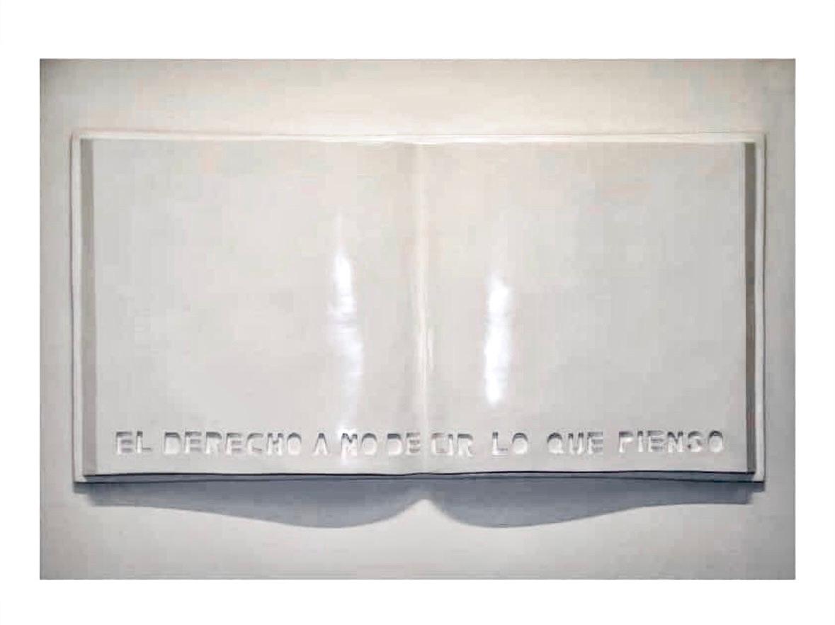 A large white sculpture of an open book with blank pages, its title in Spanish — ‘El derecho a no decir lo que pienso’ — carved along the bottom edge.
