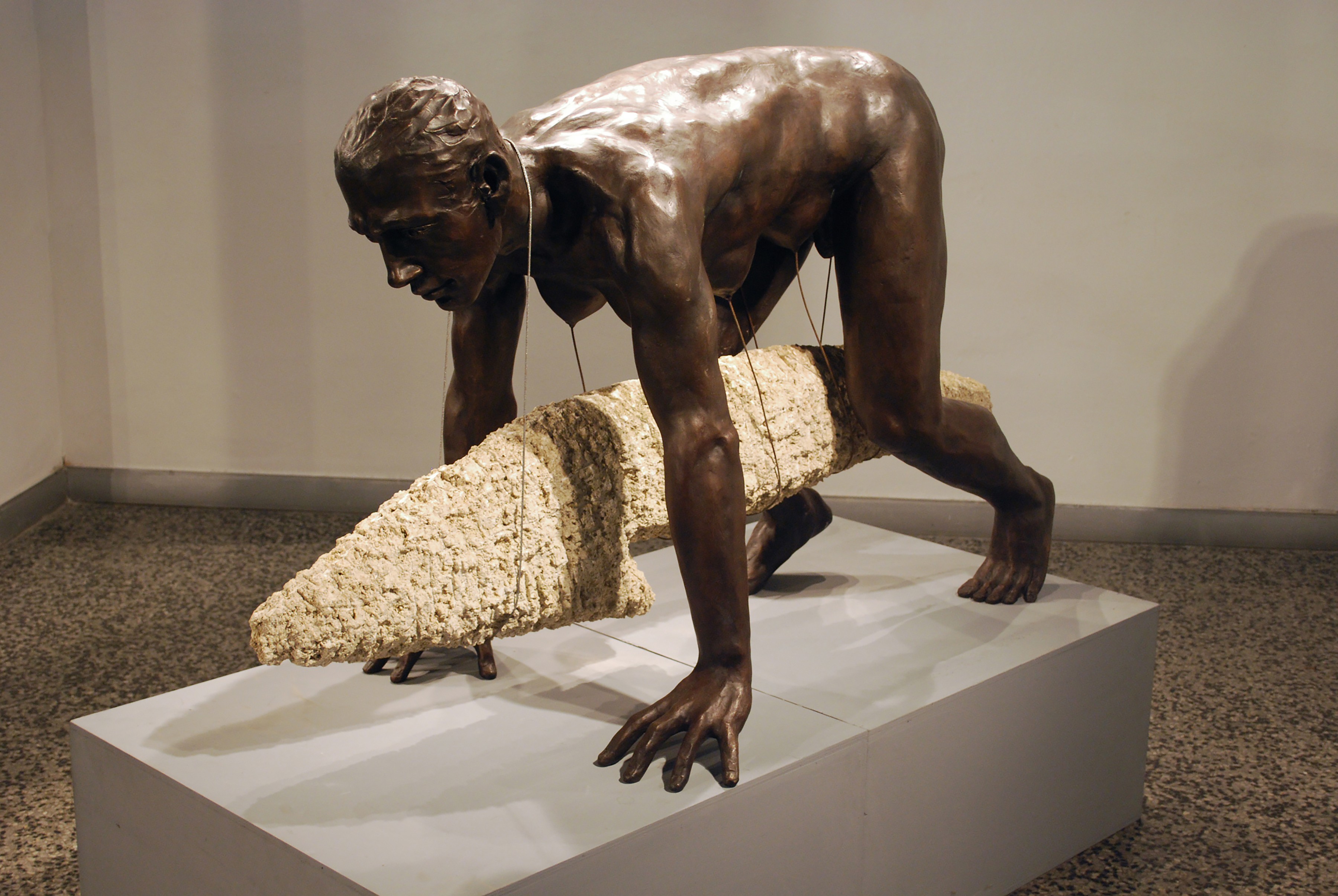 Golden bronze sculpture of a nude male figure with multiple pairs of outstretched arms radiating outward, each hand holding a small winged object, against a black background.