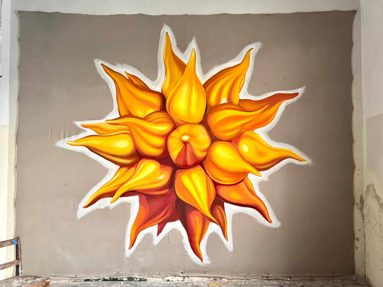 A large mural of an orange and yellow starburst-shaped form, painted on canvas in a studio.