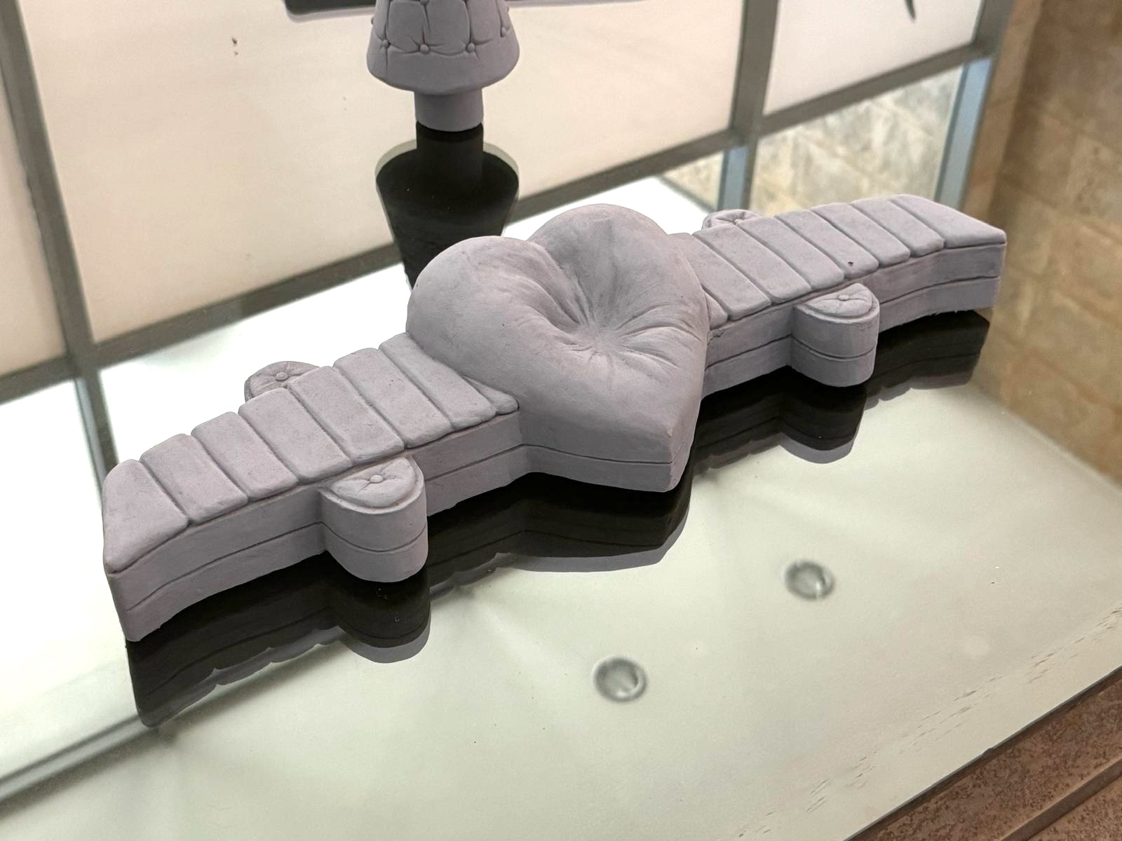 Close-up of a small clay maquette shaped like a tufted airplane-form sofa, on the glass table.
