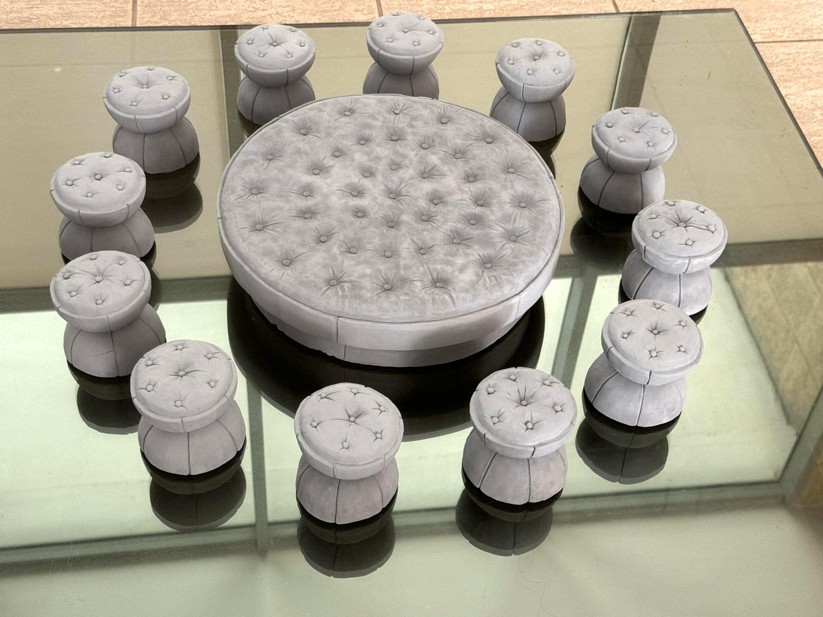 A miniature clay maquette of a round tufted table surrounded by matching tufted stool seats.