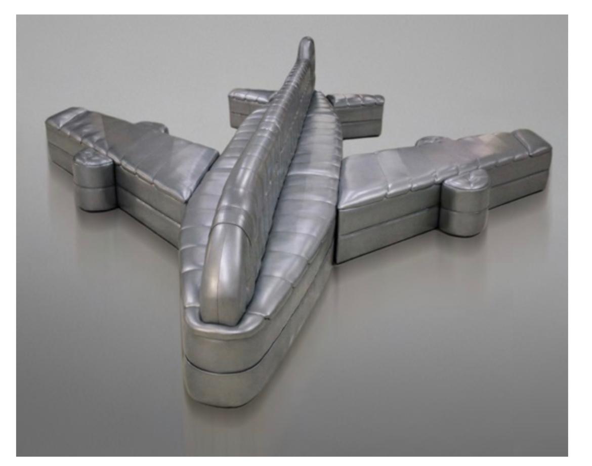 A metallic silver, airplane-shaped upholstered sofa, photographed on a reflective studio surface.