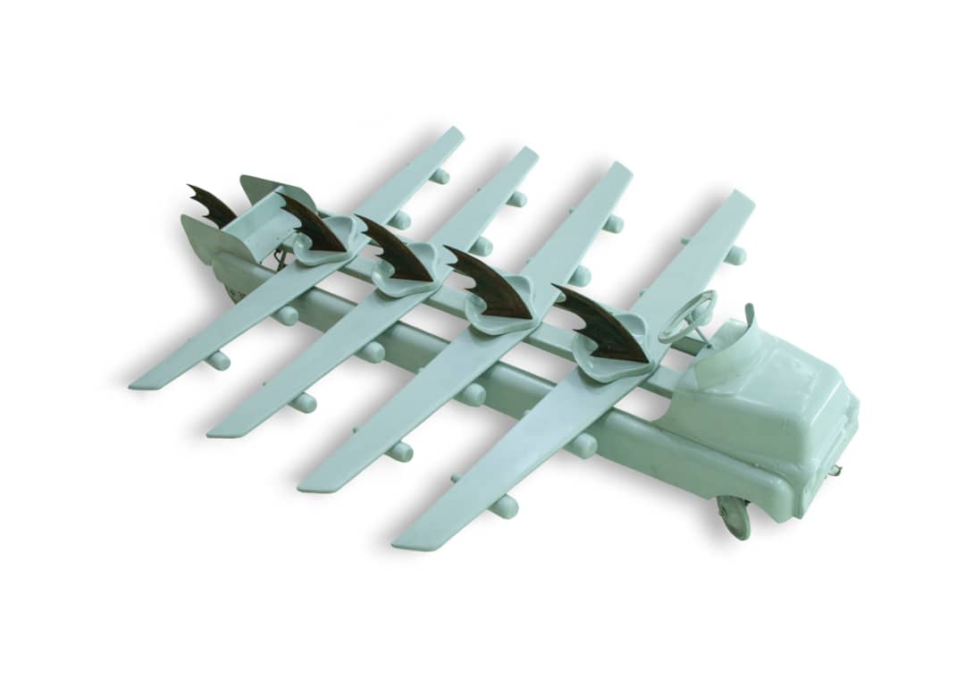 Pale mint-green sculpture of a small vintage truck cab from which radiate several long, straight wing-like blades tipped with small bat-wing fins, resembling an insect or fish.