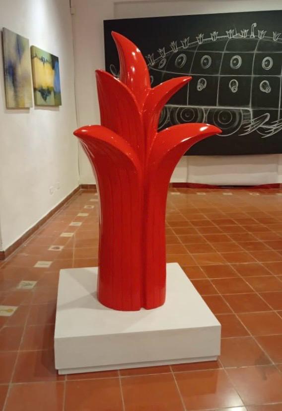 A red version of the plant-frond sculpture on a white pedestal, in a gallery with paintings and a chalkboard drawing on the wall.