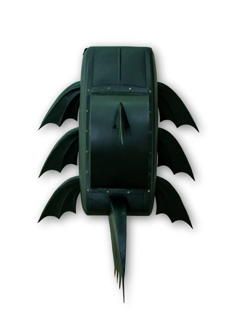 Dark green sculpture of a rounded car-like form with three pairs of bat-wing-shaped fins along each side and a fringed tail fin, photographed head-on against a plain background.