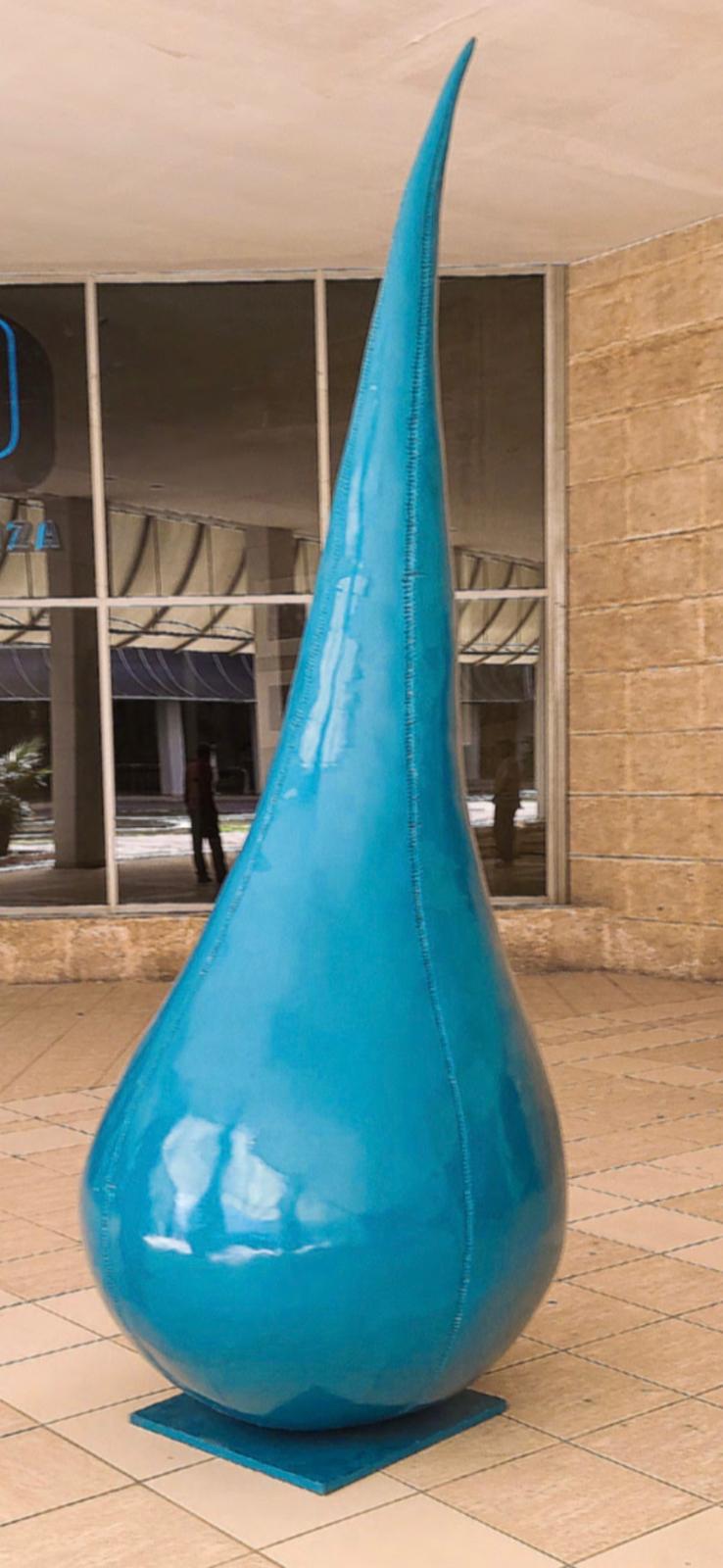 A large teardrop-shaped turquoise sculpture standing outside a building with a partial 'Plaza' sign visible.