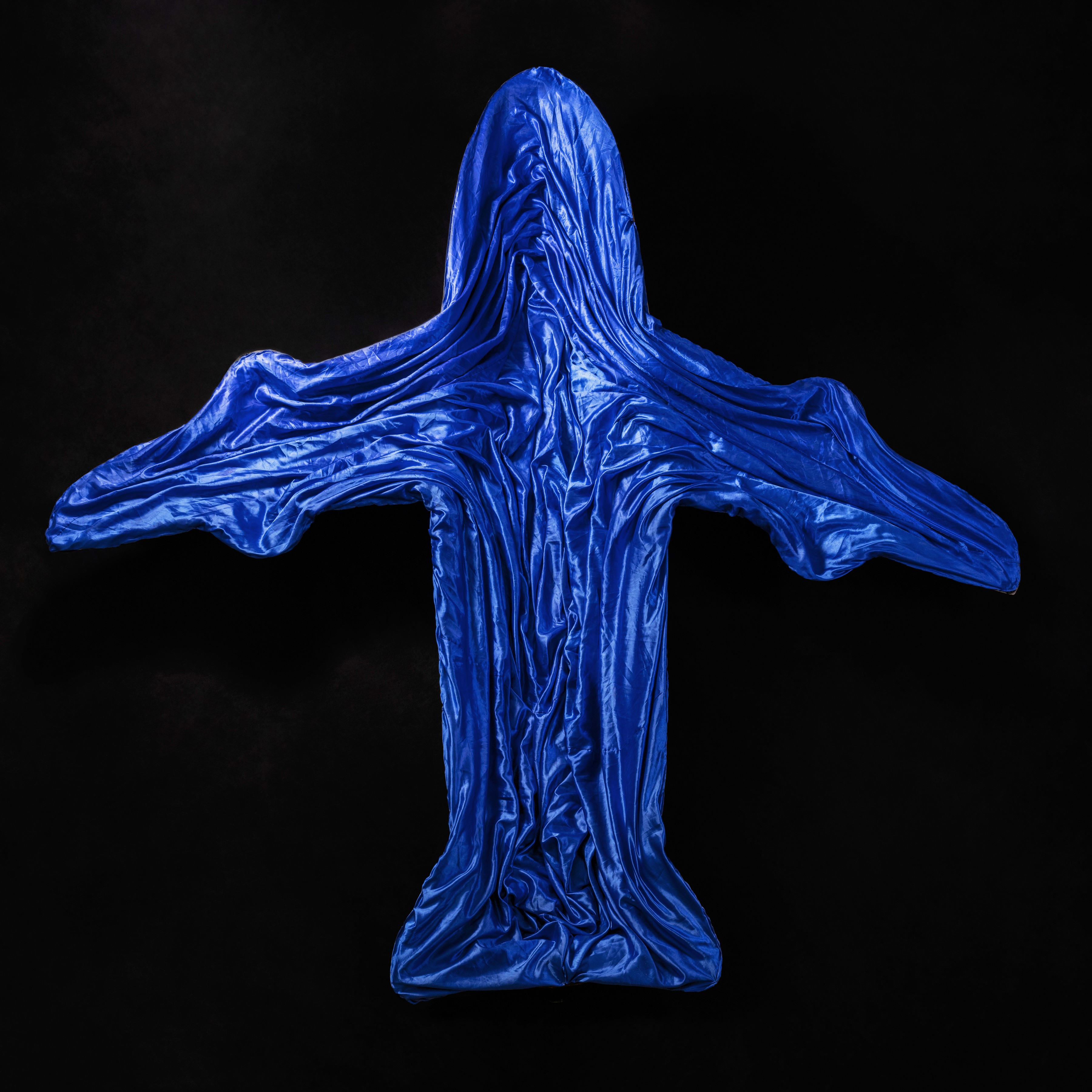 Overhead photograph of a jetliner silhouette formed from rippling blue satin fabric, its folds catching light against a black background.